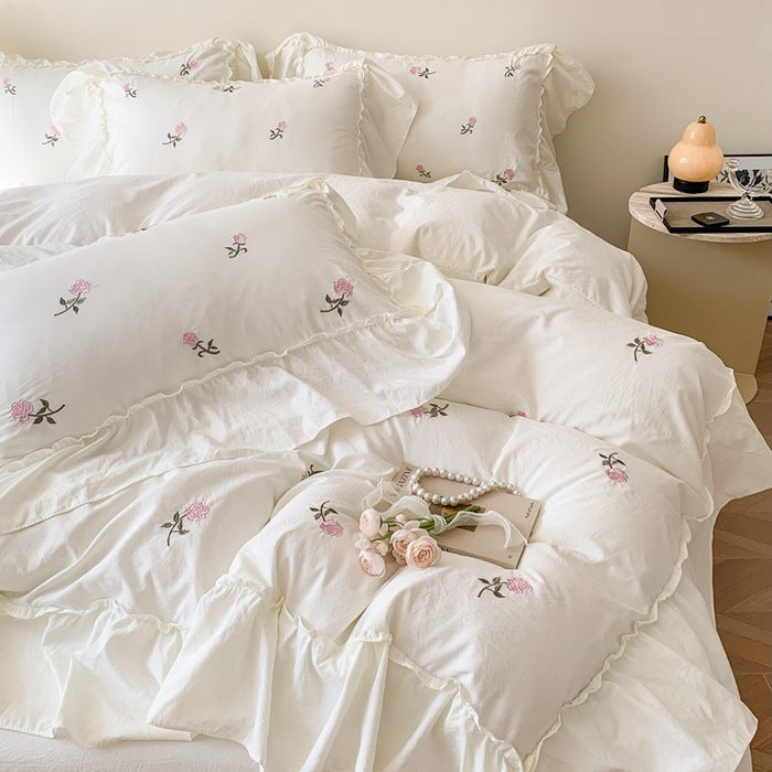 White bedding with delicate pink floral embroidery and ruffled edges